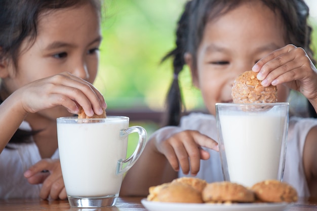 Twee leuke aziatische kleine kindmeisjes eten koekjes met melk