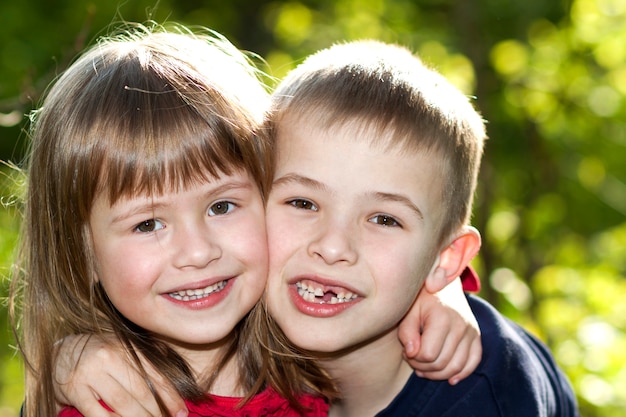 Twee leuke blonde grappige gelukkige glimlachende kinderen broers en zussen, jonge jongensbroer die zustermeisje in openlucht op heldere zonnige groene bokehaard omhelzen. Familierelatie, vriendschap en liefdeconcept.