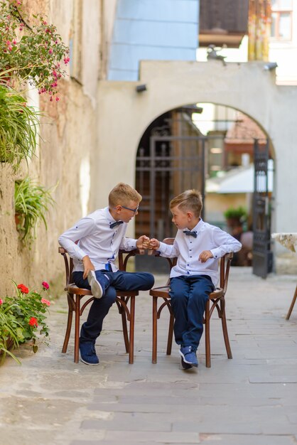 Twee leuke jongens praten zittend op houten stoelen. jongens volgen ouders na tot zakenlieden. de jongens zitten met gekruiste benen op stoelen en slaan met vuisten.