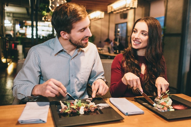 Twee lieve mensen zitten in restaurant en eten salades. ze kijken ook naar elkaar en glimlachen.