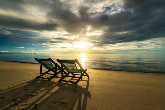 Twee ligstoelen op het strand bij zonsondergang met een tropische zee