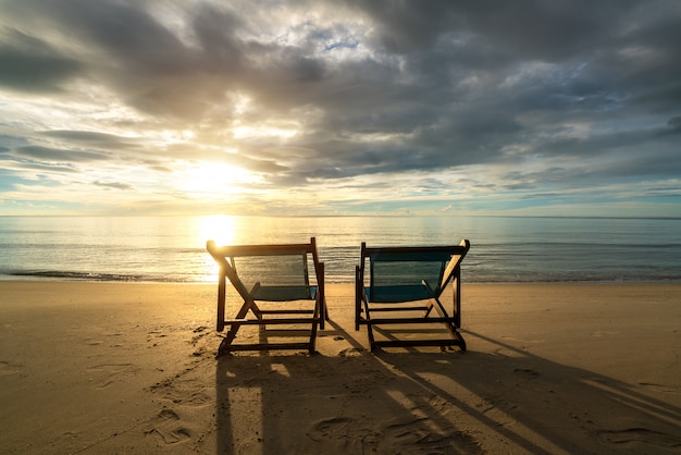 Twee ligstoelen op het strand bij zonsondergang met een tropische zee