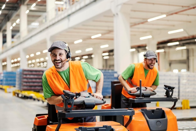 Twee magazijnmedewerkers hebben plezier op het werk door met vorkheftrucks te rijden