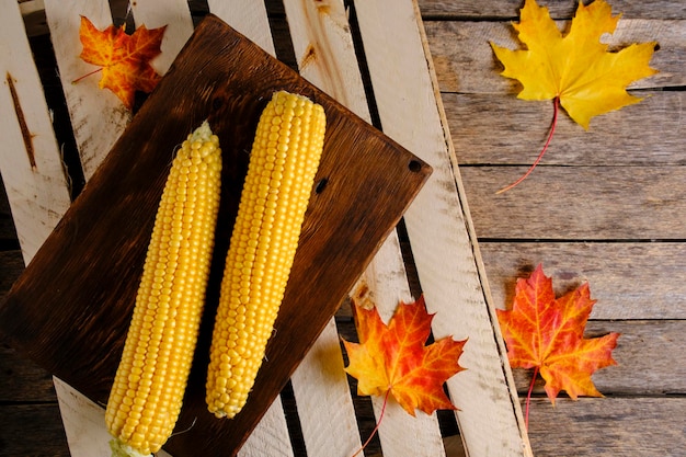 Twee maïs op houten snijplank en herfst esdoorn bladeren vallen op tafel