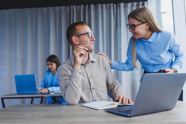 Twee manager medewerkers in een modern kantoor Europeanen man en vrouw werken aan een tafel met een laptop collega's bespreken en raadplegen nadenken over een gezamenlijk project