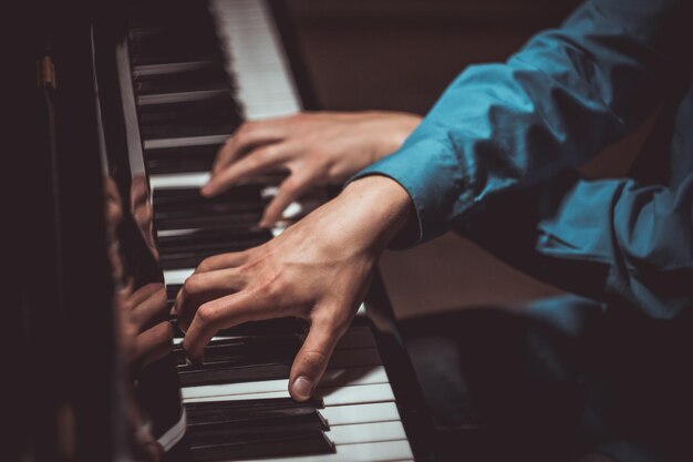 twee mannelijke handen op de piano palmen liggen op de toetsen dwars en spelen het toetsenbord instrument in de muziek school student leert om handen te spelen pianist zwarte donkere achtergrond top view