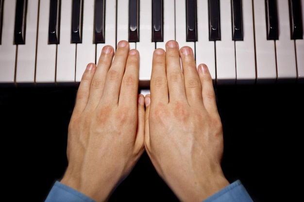 Foto twee mannelijke handen op de piano palmen liggen op de toetsen en spelen het toetsenbord instrument in de muziek school student leert om handen te spelen pianist zwarte donkere achtergrond top view