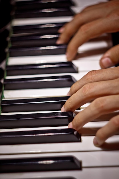 Twee mannelijke handen op de pianopalmen liggen op de toetsen en spelen het toetsinstrument in de muziekschoolstudent leert handen spelen pianist zwarte donkere achtergrond bovenaanzicht verticaal