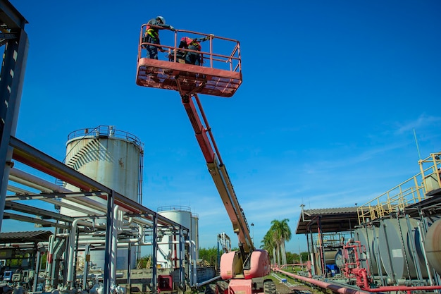 Twee mannelijke industrie werken op hoog niveau in een hoogwerkerinspectie van pijpleidingolie