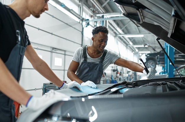 Twee mannelijke monteurs inspecteert motor, autoservice. Auto reparatie garage, mannen in uniform, auto station interieur. Professionele automatische diagnose