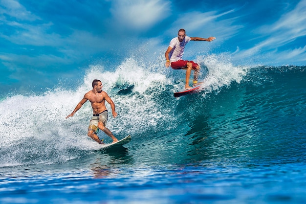 Twee mannelijke surfers op een blauwe golf op zonnige dag