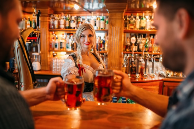 Twee mannelijke vrienden rammelende mokken met bier in de pub, serveerster aan het loket