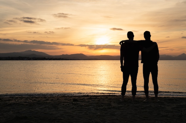 Twee mannen die elkaar met één arm vasthouden en naar de zonsondergang kijken