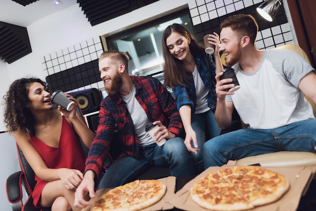 Twee mannen en twee vrouwen in opnamestudio eten pizza