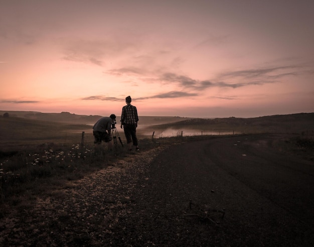 Twee mannen fotograferen bij zonsondergang tegen de hemel.