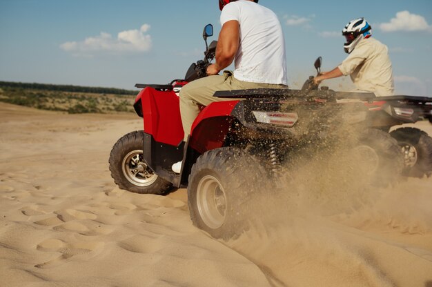 Twee mannen in helmen rijden op atv in de woestijn, achteraanzicht. Mannelijke personen op quads, zandrace, duinsafari op hete zonnige dag, 4x4 extreem avontuur, quadrijden