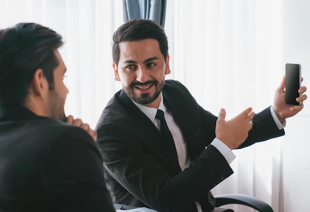 Twee mannen in pak praten met elkaar voor een raam.