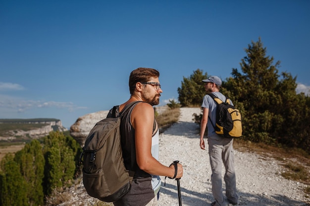 Twee mannen lopen op een rotsachtige helling en dragen rugzakken met trekkingstokken