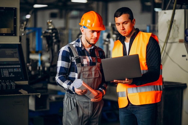 Twee mannen met oranje vesten werken aan een laptop.