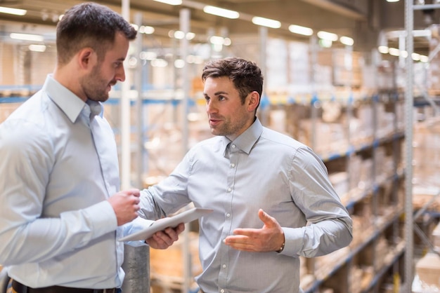 Twee mannen met tablet praten in fabrieksmagazijn