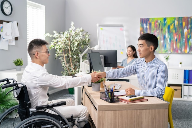 Twee mannen ontmoeten elkaar in het kantoor van het bedrijf 's ochtends voor interview jongen met handicap arriveert in rolstoel