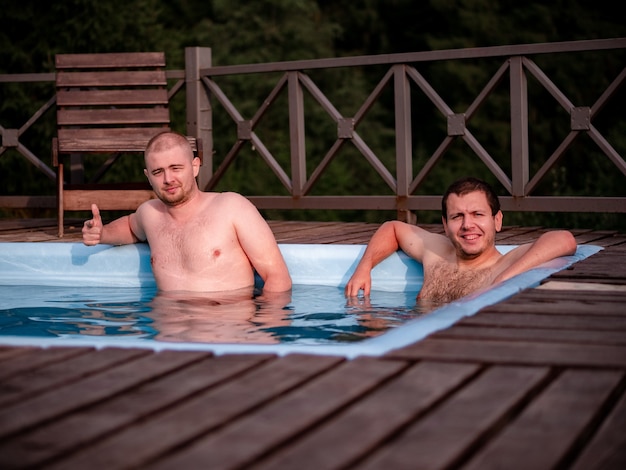 Twee mannen rusten in het zwembad tegen de achtergrond van het bos, een van hen wijst met een vinger