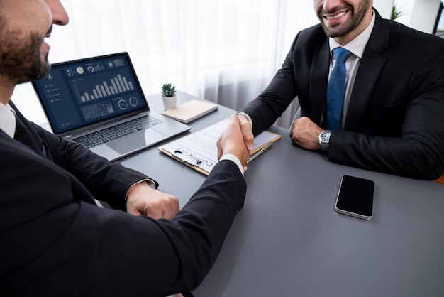 Twee mannen schudden elkaar de hand met een laptop op tafel