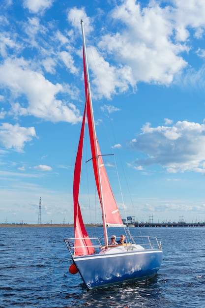 Twee mannen zeilen op een klein jacht met scharlaken zeilen op het stuwmeer