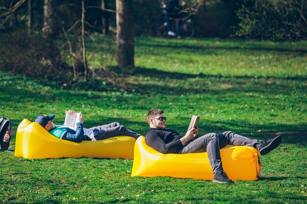 Twee mannenvrienden die op gele opblaasbare matrassen liggen om boeken te lezen