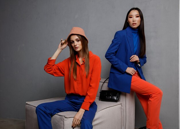 Foto twee mannequins in blauworanje outfits jasje blazer overhemd broek broek handtas hoed