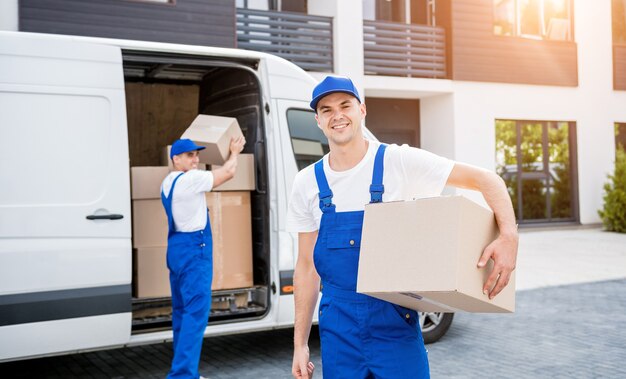 Twee medewerkers van het verhuisbedrijf lossen dozen van minibus in nieuwe woning