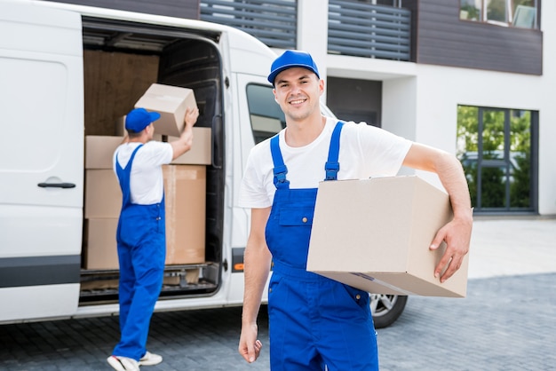 Twee medewerkers van het verhuisbedrijf lossen dozen van minibus in nieuwe woning