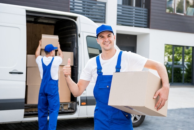 Twee medewerkers van het verhuisbedrijf lossen dozen van minibus in nieuwe woning