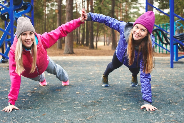 Twee meisjes atleten in de sport doen fysieke oefeningen op de buitenspeeltuin in het bos. Een gezonde leefstijl