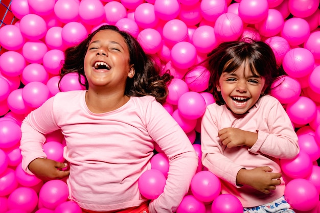 Twee meisjes die en bij roze ballenpool glimlachen spelen