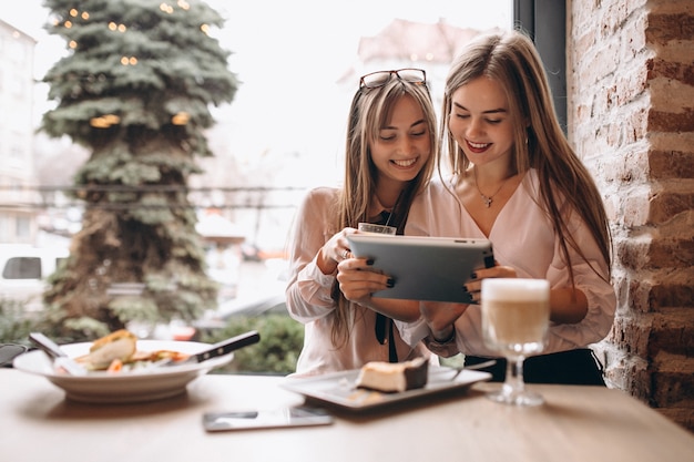 Twee meisjes die op tablet in een koffie winkelen