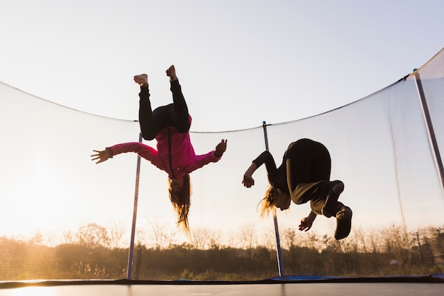 Foto twee meisjes die op trampoline bij zonsondergang springen