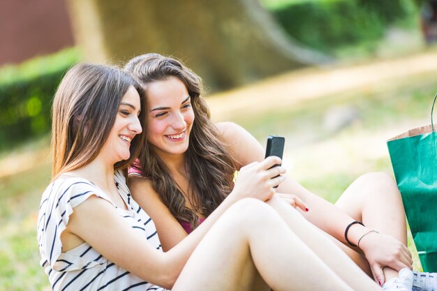 Twee meisjes die slimme telefoon bekijken bij park