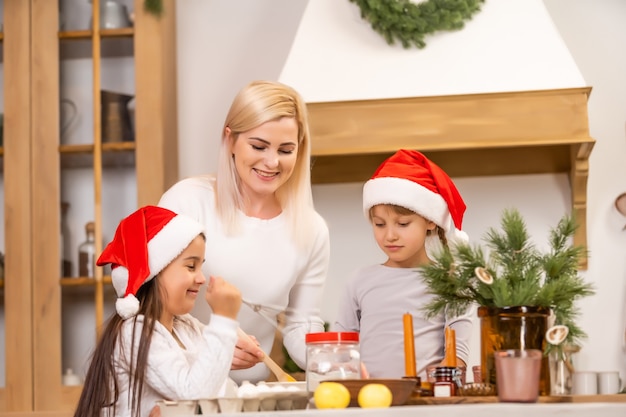 Twee meisjes gekleed in rode hoeden bereiden koekjes, peperkoek voor de nieuwjaarsvakantie, Kerstmis. Knip koekjes uit.