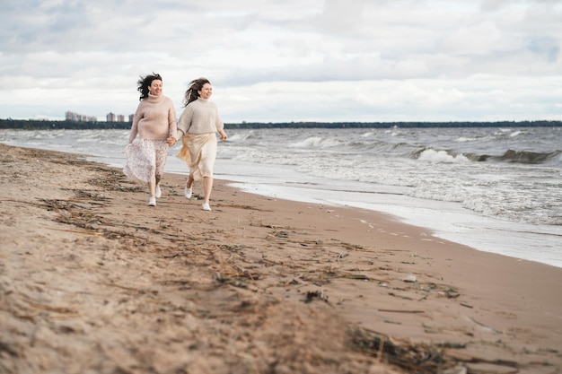 Foto twee meisjes houden elkaars hand vast en rennen langs de kust, de zussen hebben plezier samen een verliefd stel op een