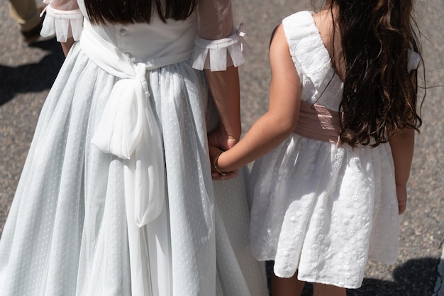 Twee meisjes houden elkaars hand vast terwijl ze in hun witte jurken lopen