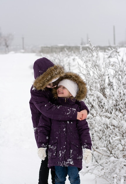 Twee meisjes in identieke jassen staan te kletsen op een besneeuwd veld tijdens een sneeuwval, ze kijken elkaar aan en glimlachen