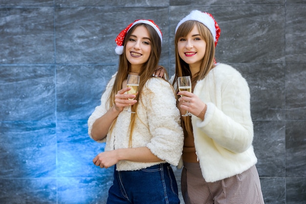 Twee meisjes in kerstmutsen met champagneglazen vieren nieuwjaar