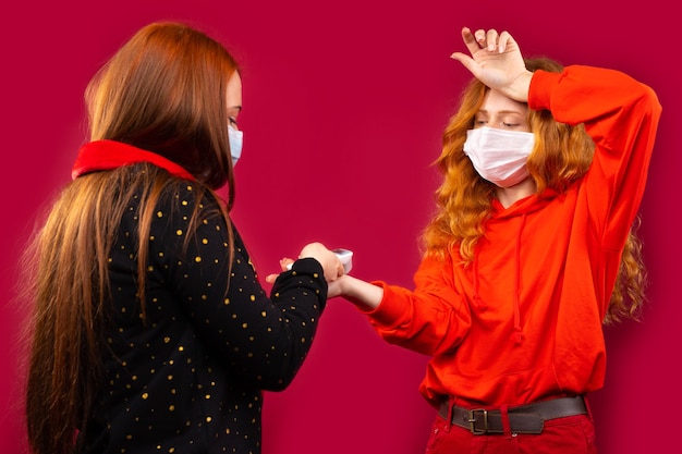 Twee meisjes in medische maskers meten hun lichaamstemperatuur met een contactloze thermometer. foto op een rode muur.