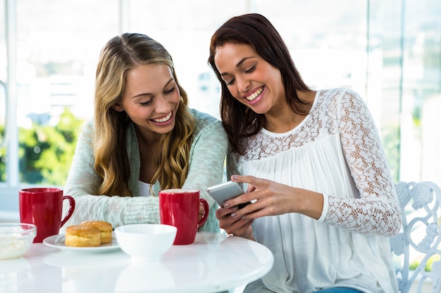 twee meisjes kijken naar een telefoon terwijl ze eten en drinken