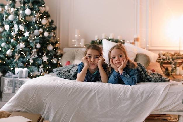 Twee meisjes liggen op het bed in het interieur van de kerstkamer. de vooravond van de vakantie