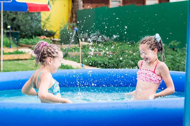 Twee meisjes met afro-vlechten hebben plezier met opspattend water in een opblaasbaar zwembad op een zomerse dag in de achtertuin