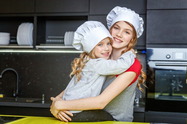 Twee meisjes met chef-kokhoed die en pret in keuken koesteren hebben