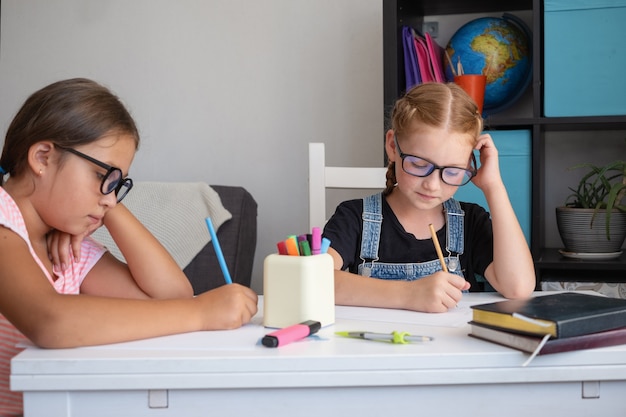 Twee meisjes met een bril die thuis studeren, maken huiswerk. Schrijven. nerd. Terug naar schoolconcept.