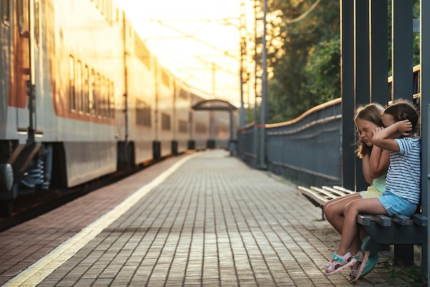 Twee meisjes op de bank van het station en van angst bedekten ze hun oren met hun handen